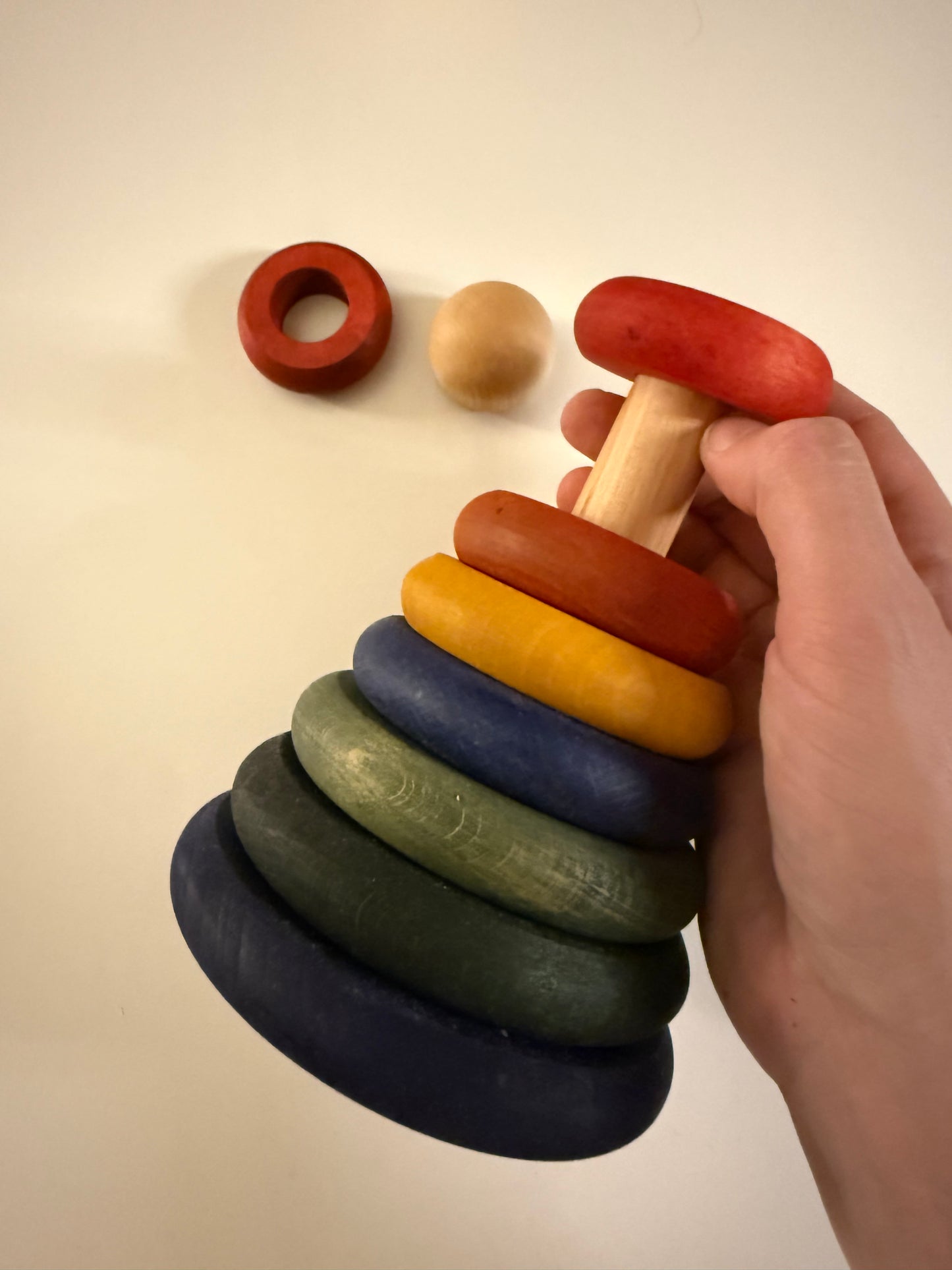 Kinderhand stapelt bunte Holzringe – Montessori Stapelspiel fördert Motorik